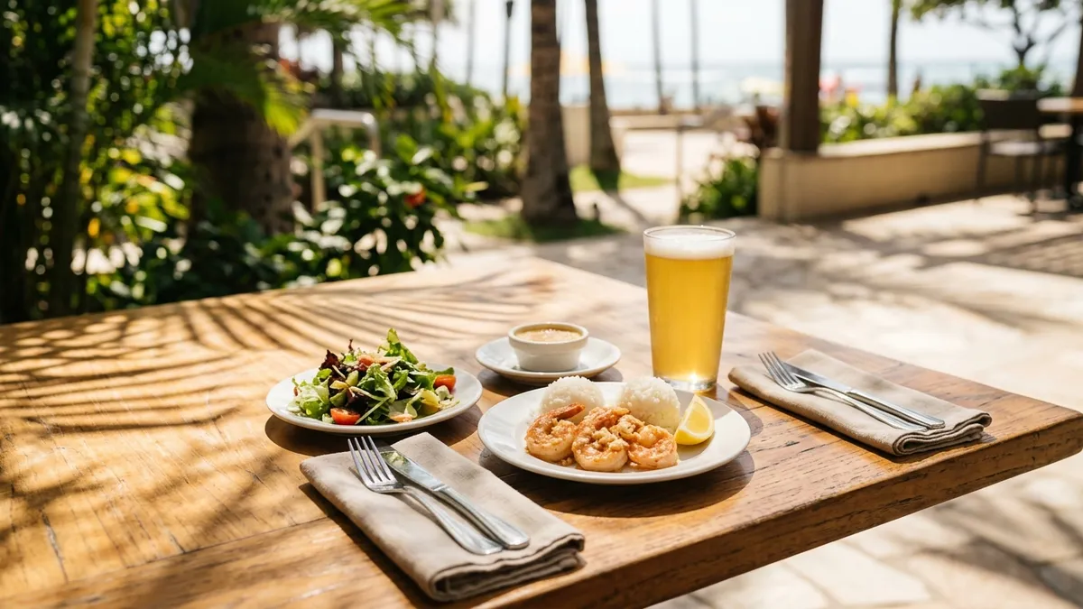 A small three-course lunch set on an open-air cafe table in afternoon light, with a pint of pale beer beside the plates and palm shadows on the floor